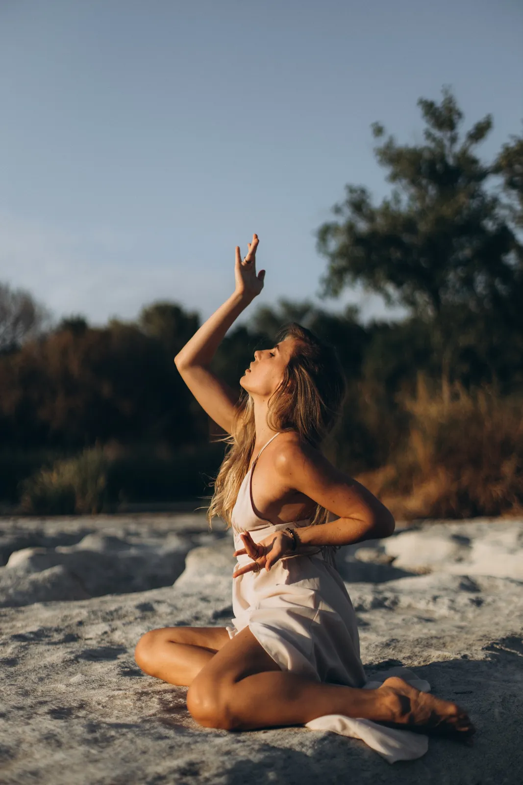 Julia seated on the river rocks with one arm raised toward the sky