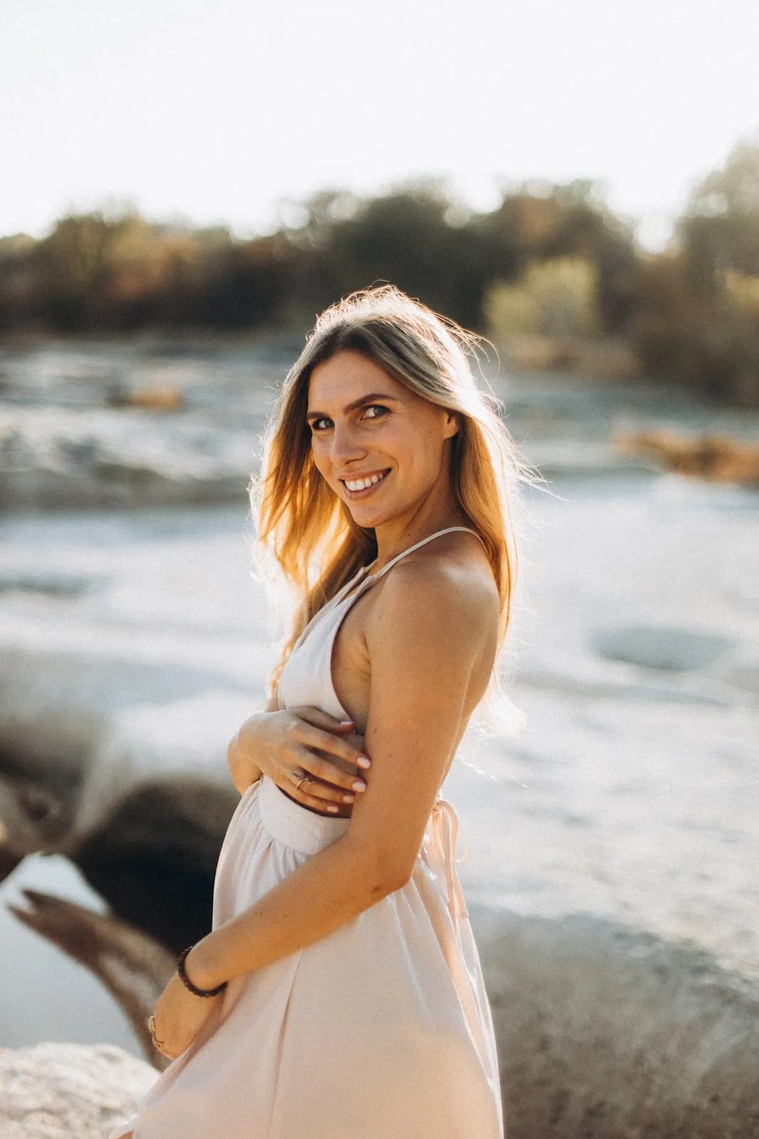 Julia Eske smiling in a long cream dress on the limestone riverbank at golden hour