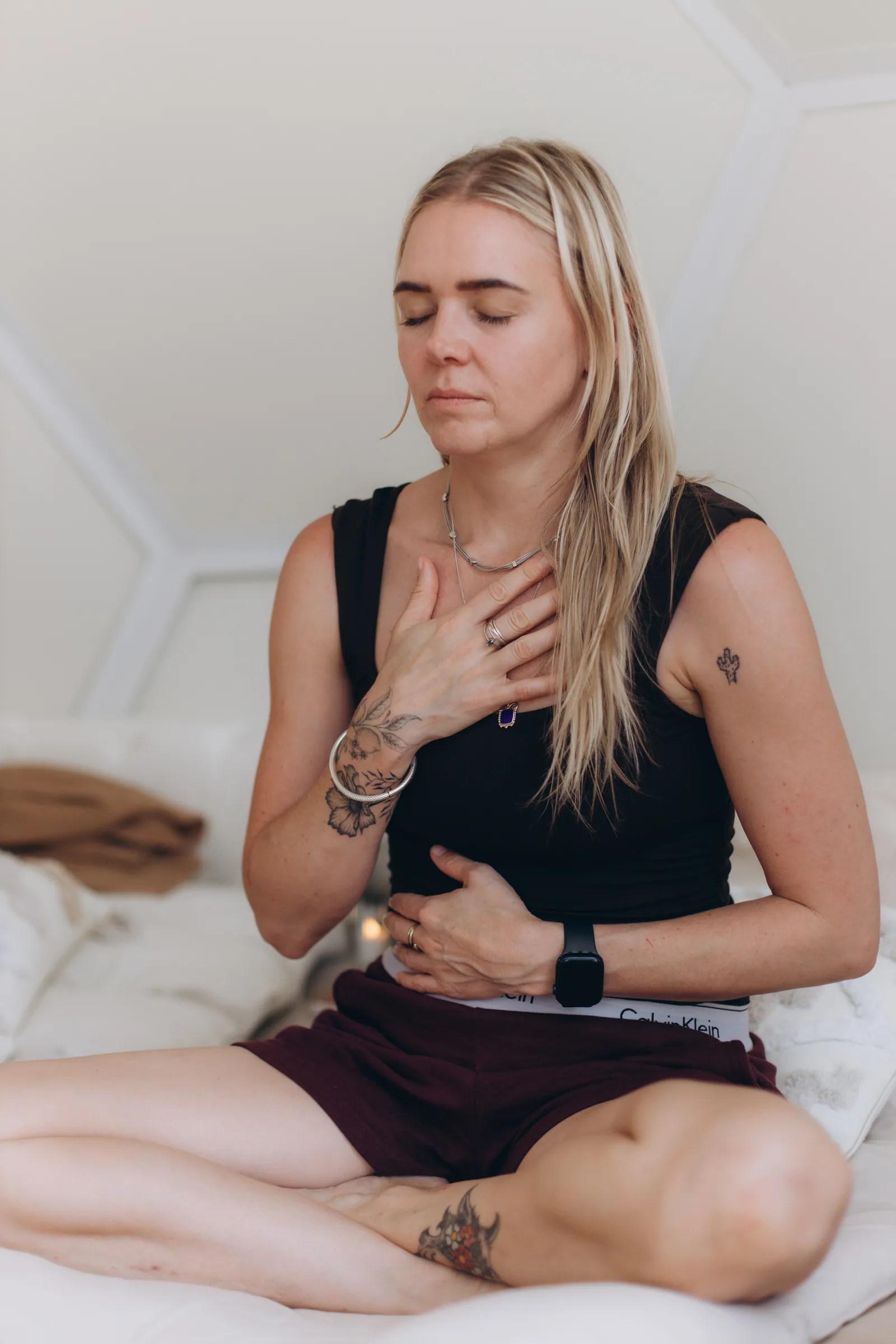 A woman seated with one hand on her heart and one on her belly
